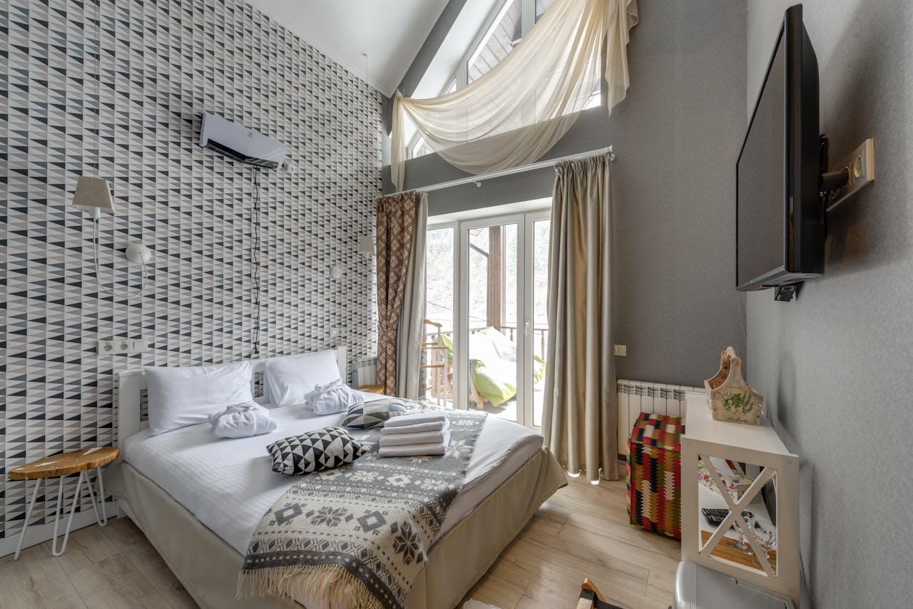 Bright and cozy modern bedroom featuring large windows, TV, and stylish decor.